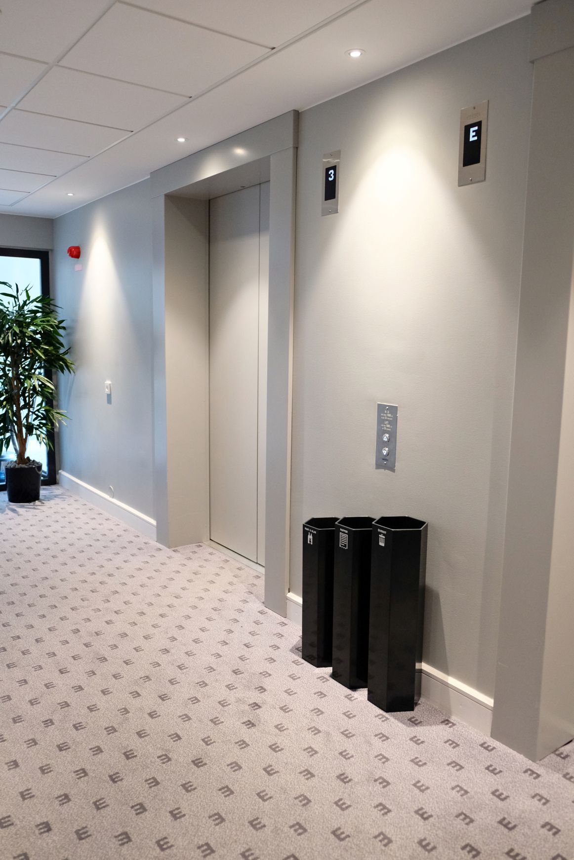 Tre svarta Sortify Papaya-kärl vid hisshallen i en hotellobby